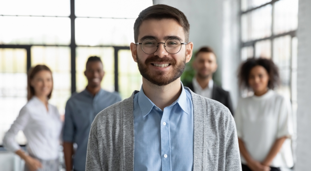 Head shot portrait of a smiling businessman with team members behind him